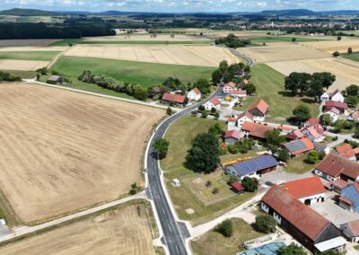 Luftaufnahme von Reckenstetten: rote Dächer, kurvenreiche Straße, Ackerland, bewölkter Himmel.