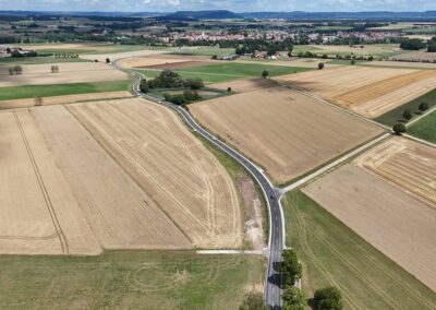 Luftaufnahme von zusammengewürfelten Feldern, kurvenreicher Straße, Bäumen und dem entfernten Freystadt.