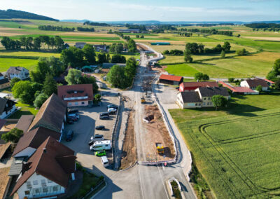 Luftaufnahme: ländlicher Straßenbau, Maschinen, Häuser und grüne Felder.