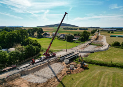 Kran und Fahrzeuge bauen eine Brücke im ländlichen Freystadt, dahinter Felder.